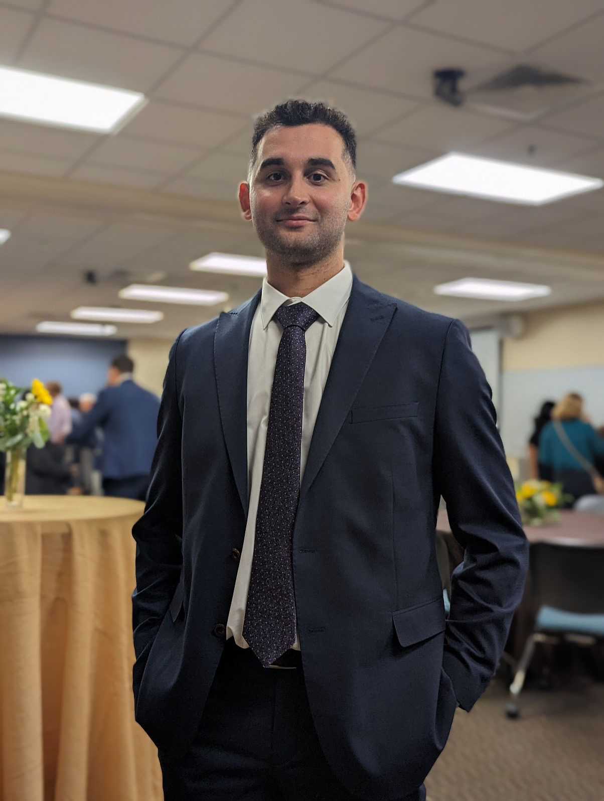 Emre Can Aslan at an academic conference event, wearing a navy suit and tie